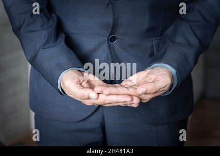 Close-up side view of the hands of an unidentified young man in shirt and jacket holding an invisible object on palm. The concept of caring hands. Adv Stock Photo