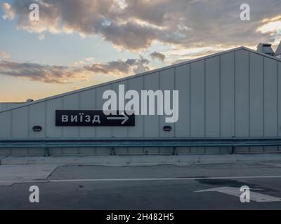 Directional exit right arrow sign in black and white on the metal wall at the rooftop parking of a shopping mall in the evening. Sign: EXIT, Ukrainian Stock Photo