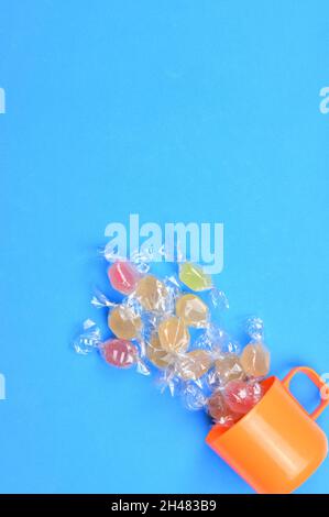 Vertical top view of glass candies falling out of an orange mug on a blue background with copy space Stock Photo