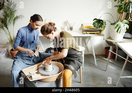 Portrait of two young women working on pottery wheel together in handmade ceramics workshop, copy space Stock Photo