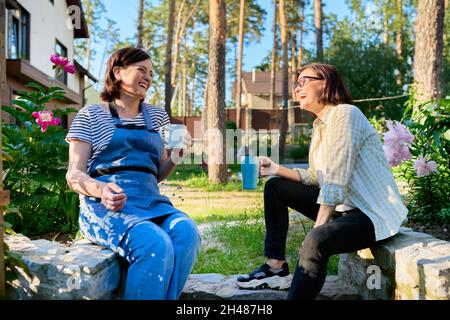Two middle aged women sitting outdoors together in garden, backyard with mugs of tea Stock Photo