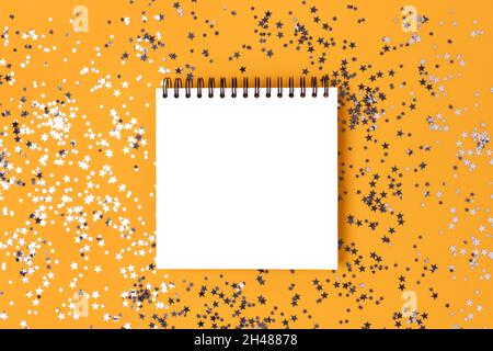 Blank square notepad mockup with glittering silver stars confetti on a yellow background. Stock Photo