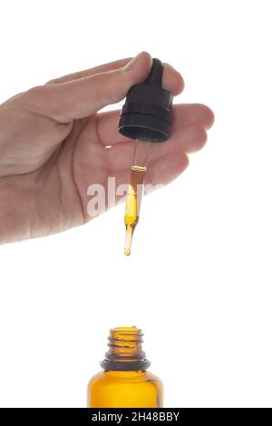 Woman holding pipette with natural oil over glass bottle. Woman's hand holds mock-up of dropper bottle isolated on white background.