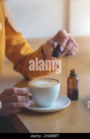 Woman using cannabis plants in drinks. Adding CBD oil in a coffee cup.The concept of using medical marijuana. Stock Photo