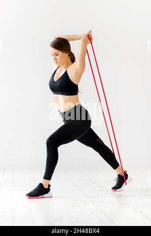 Woman doing power band fitness exercises to strengthen and stretch her body muscles over a high key background in a gym in a health and fitness concep Stock Photo