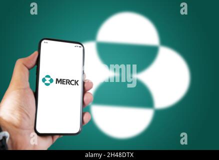 New York, USA, October 2021: A hand holding a phone with the Merck pharmaceutical company app on the screen and Merck logo blurred on a green backgrou Stock Photo