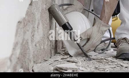 house renovation concept, hands of construction worker with gloves takes the helmet near compressor and pneumatic air hammer chisel, close up on floor Stock Photo