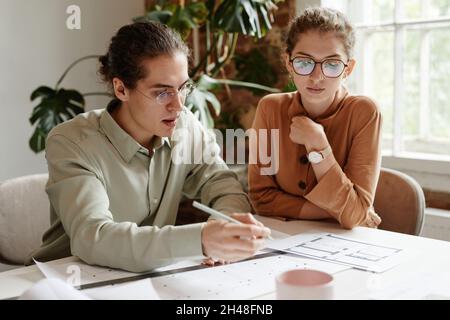 Portrait of two young architects discussing floor plan project at team meeting Stock Photo