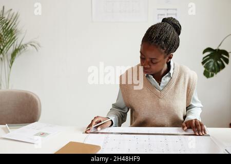 Portrait of young African-American woman inspecting floor plans while working at architects office, copy space Stock Photo