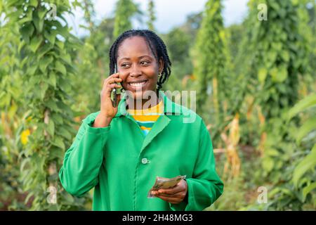 Shot of a happy female African farmer in Nigeria making a phone call, holding some money Stock Photo