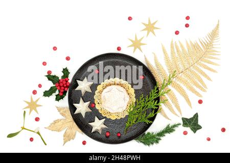 Luxury Christmas mince pie treat on plate with gold leaf, star tree decorations, holly, loose berries and winter flora on white background. Stock Photo