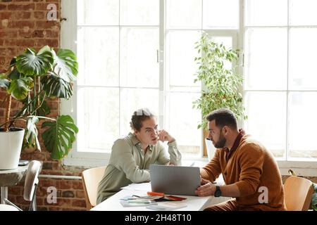 Wide angle portrait of two creative people using laptop while discussing design project in studio, copy space Stock Photo