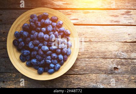 Plate with plums on a rustic wooden background, top view Stock Photo