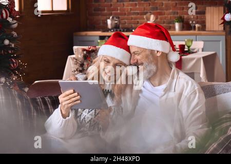 Happy old couple using digital tablet feeling joy have virtual Christmas party. Stock Photo