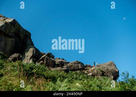 People pointing from a viewpoint on the Cow and Calf Rocks with the moon in the sky, West Yorkshire, UK Stock Photo