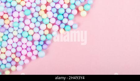 Foam beads of various colors brightly colored on pink pastel background with empty space. Stock Photo
