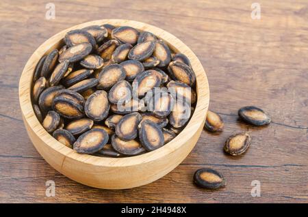 Black dry watermelon seeds in wooden bowl on the table. Stock Photo