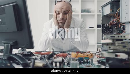 Stressed frustrated computer repair technician sitting at office desk with head in hands Stock Photo