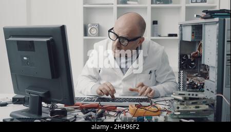 Computer repair technician, working on a PC, he is typing on a keyboard and looking at the computer screen Stock Photo