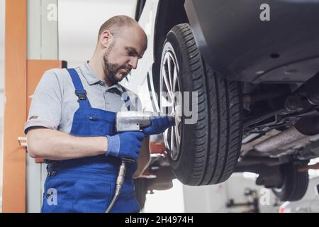 Professional mechanic doing a wheel replacement on a lifted car using a pneumatic wrench Stock Photo