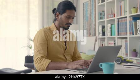 Indian man sitting at desk and typing with his laptop, he is working from home Stock Photo