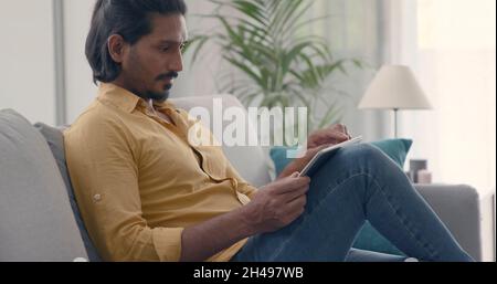 Man relaxing on the sofa at home, he is connecting online and using apps on his digital tablet, lifestyle and technology concept Stock Photo