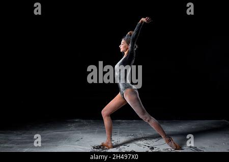 Dancing in flour concept. Slim beautiful female adult woman dancer in dust, fog. Lady is wearing black bodysuit, making dance element gracefully on is Stock Photo