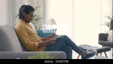 Handsome man sitting on the couch at home and connecting with a digital tablet, lifestyle and technology concept Stock Photo