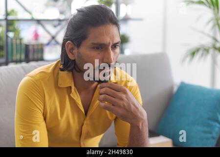 Indian man sitting on the couch at home and thinking with hand on chin Stock Photo