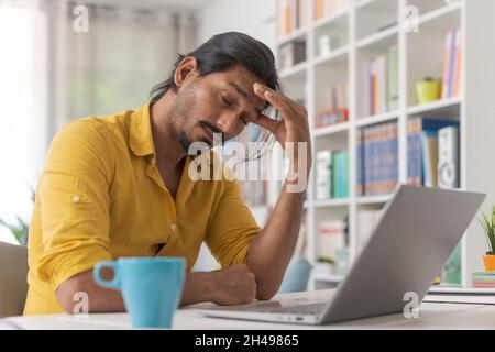 Young stressed man working with a laptop in his office at home, he is having a bad headache Stock Photo