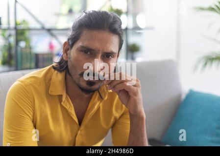 Indian man sitting on the couch at home and adjusting his moustache Stock Photo