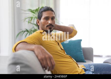 Confident handsome young man relaxing on the couch at home and looking at camera Stock Photo