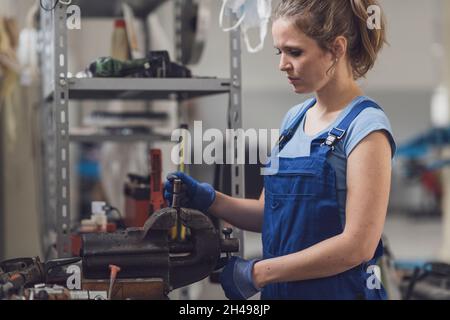 Professional confident female mechanic working in the garage, she is using a bench vise Stock Photo