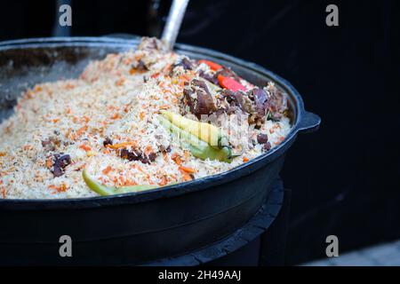 Rice with meat, carrots in a large cauldron. Pilaf with spices during the Christmas market. Street food - pilaf in a black pot. Stock Photo