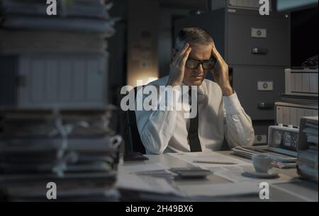 Stressed businessman working until late and having a headache Stock Photo