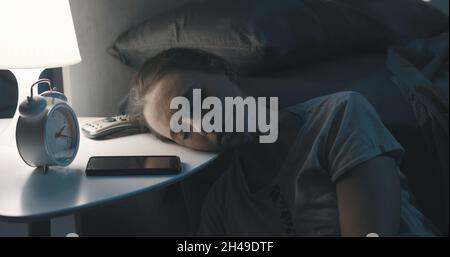 Exhausted woman lying her head on the bedside table and sleeping late at night Stock Photo