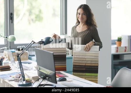 Interior designer holding fabric swatches in her studio, she is smiling at camera Stock Photo