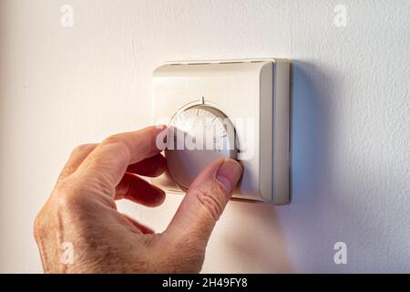 Hand adjusting the temerature on a wall mounted thermostat. Central heating. Stock Photo