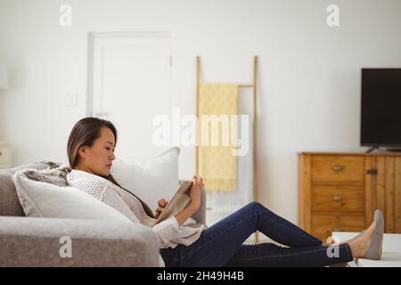 Focused asian woman sitting on sofa with tablet at home Stock Photo