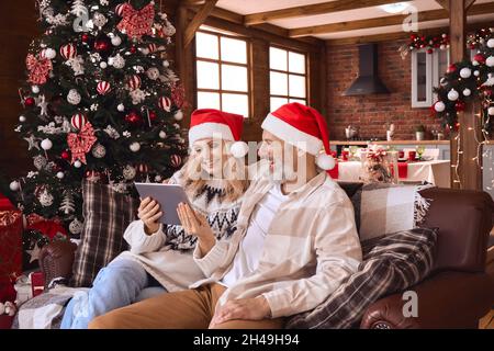 Happy 50s older couple using digital tablet in living room on Christmas. Stock Photo