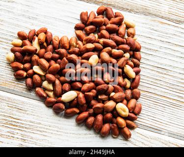 Peeled peanuts in a shape of heart on a white wooden background Stock Photo