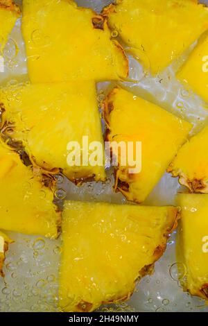 Pineapple close-up in liquid with bubbles. Slices of ripe pineapple in water. Close-up fresh slices of yellow pineapple on white background. Vertical Stock Photo