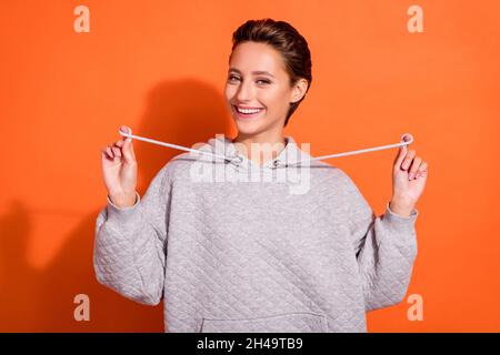 Photo of pretty sweet young lady wear grey sweatshirt smiling isolated orange color background Stock Photo