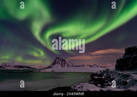 Aurora Borealis in the Lofoten Islands, Norway. Northern lights dancing on the sky. Snowy mountains and the sea coast Stock Photo