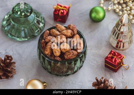 Candied or sugared almonds with honey and cinnamon in trendy green small glass jar on gray with Christmas decoration background. Traditional Christmas sweets for holidays. Copy space Stock Photo