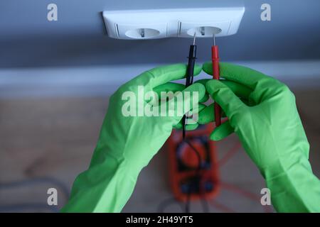 Craftsman in rubber gloves holding tester near electrical outlet at home closeup Stock Photo