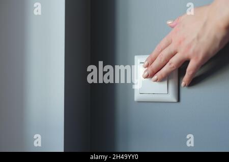 Female hand pressing light switch in apartment closeup Stock Photo