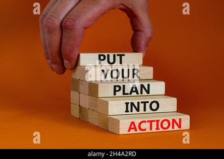 Put your plan into action symbol. Wooden blocks with words Put your plan into action. Beautiful orange background, copy space. Businessman hand. Busin Stock Photo