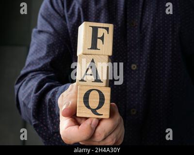 Man holds cubes with world FAQ frequently asked questions. Stock Photo