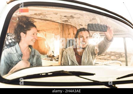 Indie couple ready for roadtrip on oldtimer mini van transport - Travel lifestyle concept with young hippie people having fun traveling on minivan Stock Photo